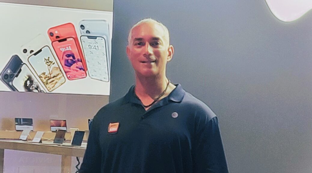 Curtis Matthews standing in a tech store in front of a digital display of various smartphone models.